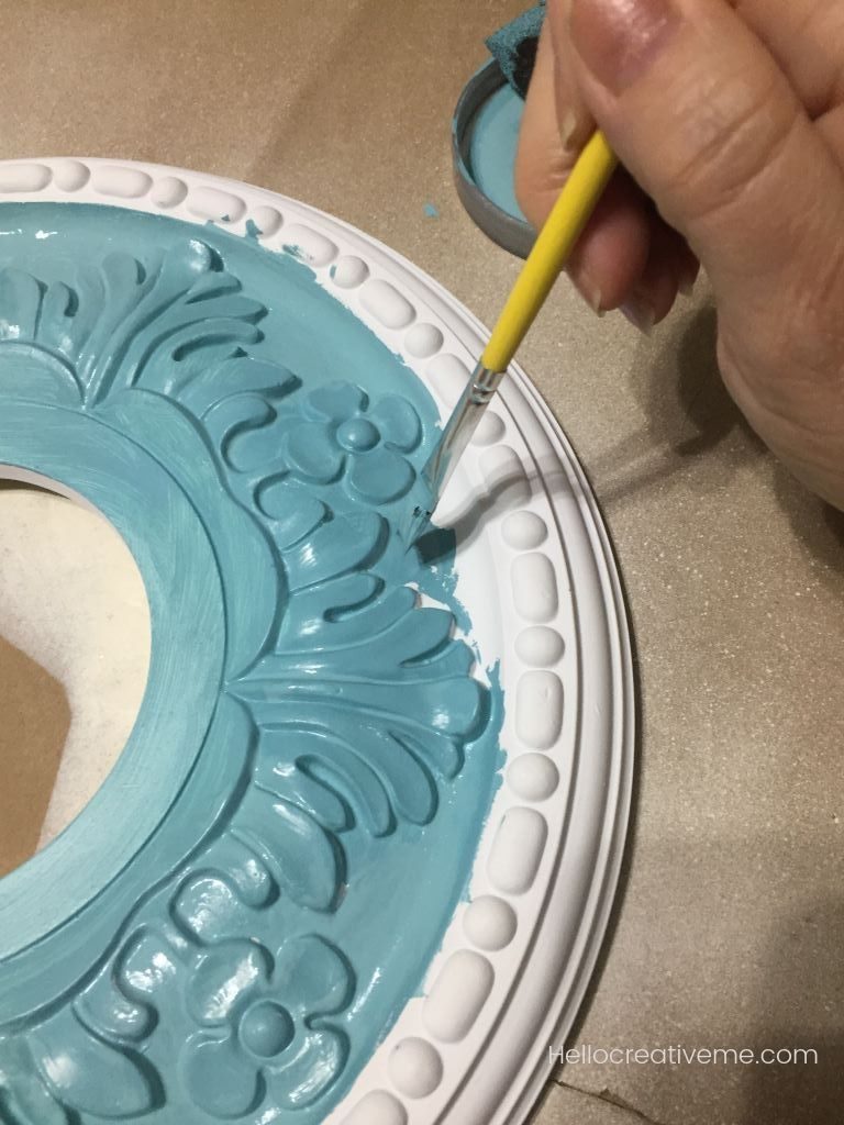 woman painting ceiling medallion with aqua paint
