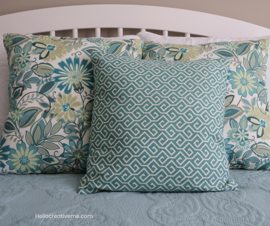 3 aqua floral and geometric pillows on a bed