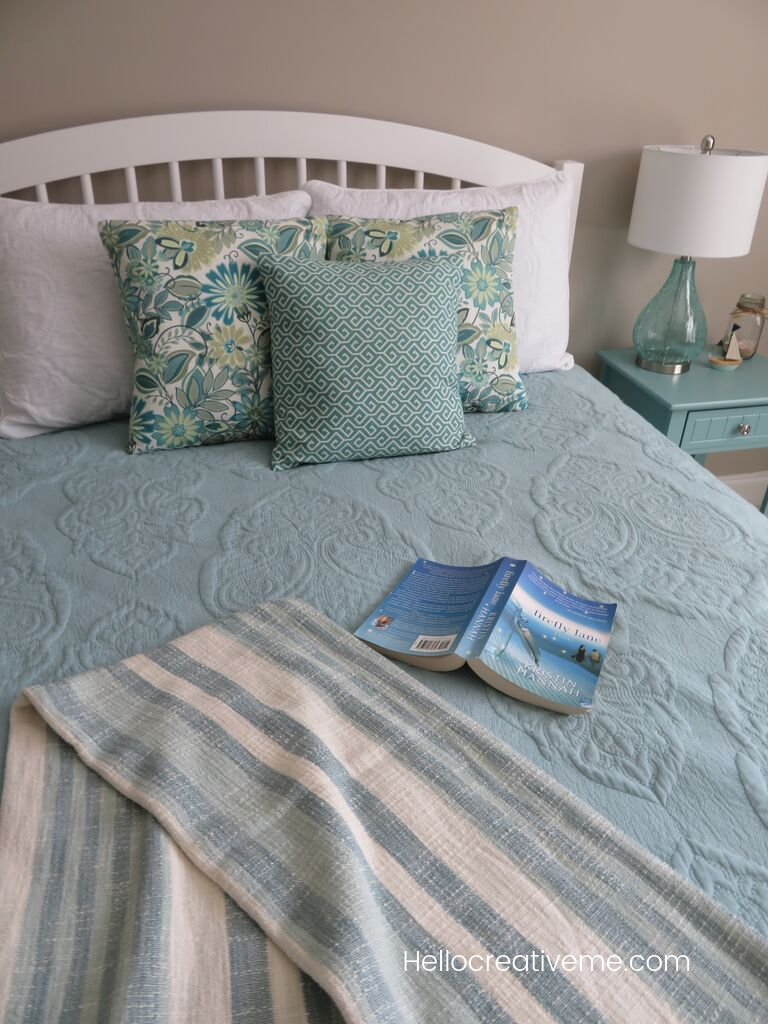 blanket and book draped over aqua quilt on queen bed