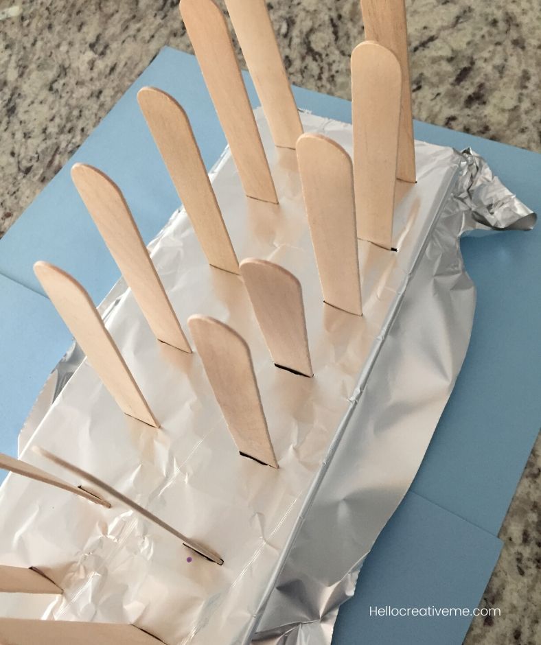 ice cube tray covered in foil with popsicle sticks in it