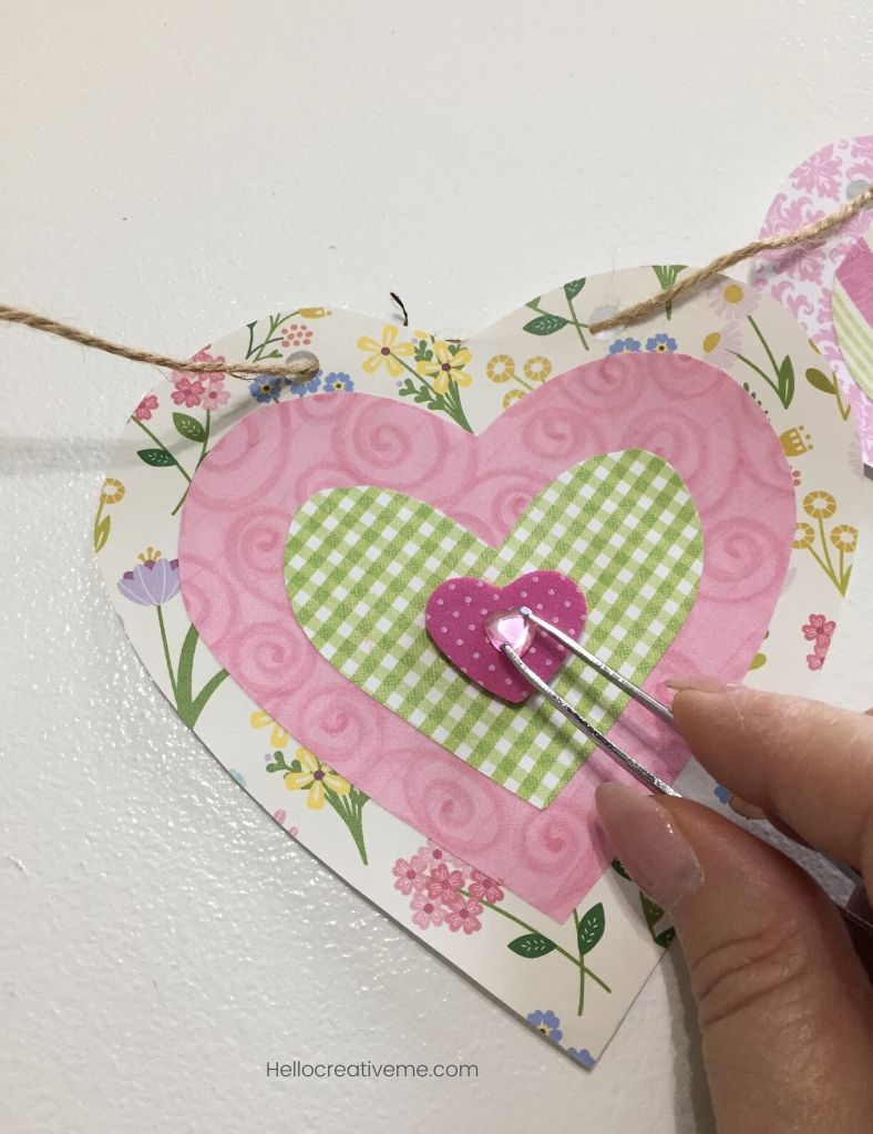 Tweezers placing tiny jewel sticker on paper heart