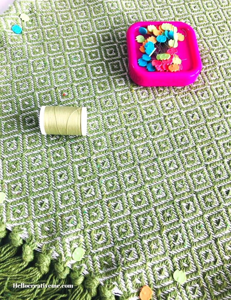 green thread and pins in pink holder on top of throw rug