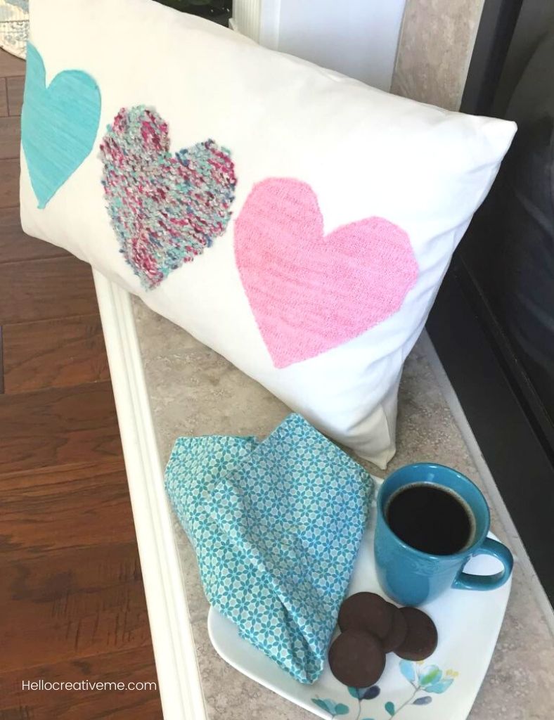 3 valentine hearts on lumbar pillow next to coffee and cookies on a plate