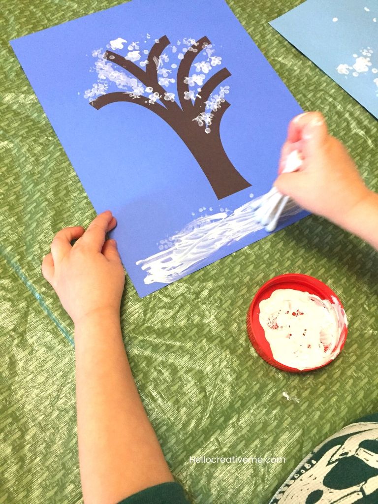Child applying white paint to winter tree template