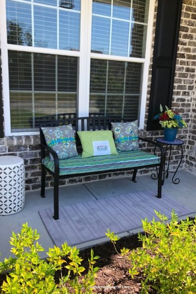 black porch bench with decorative pillows in front of window