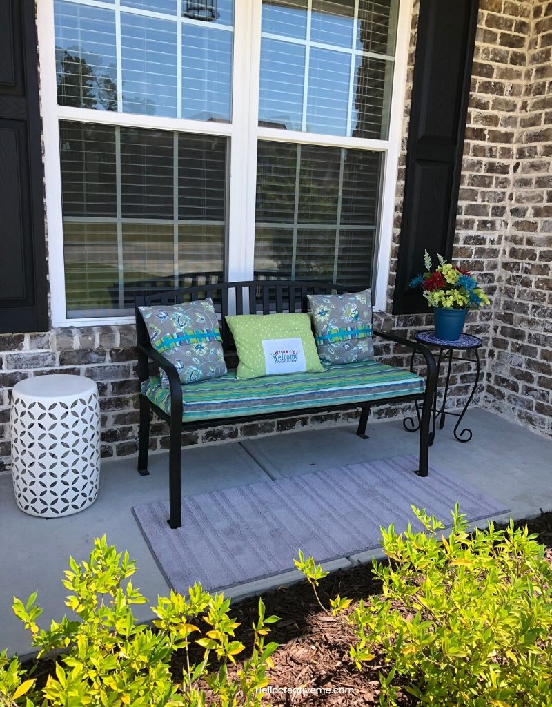 Refreshed spring front porch decor with black bench, teal pillows, and colorful flowers.