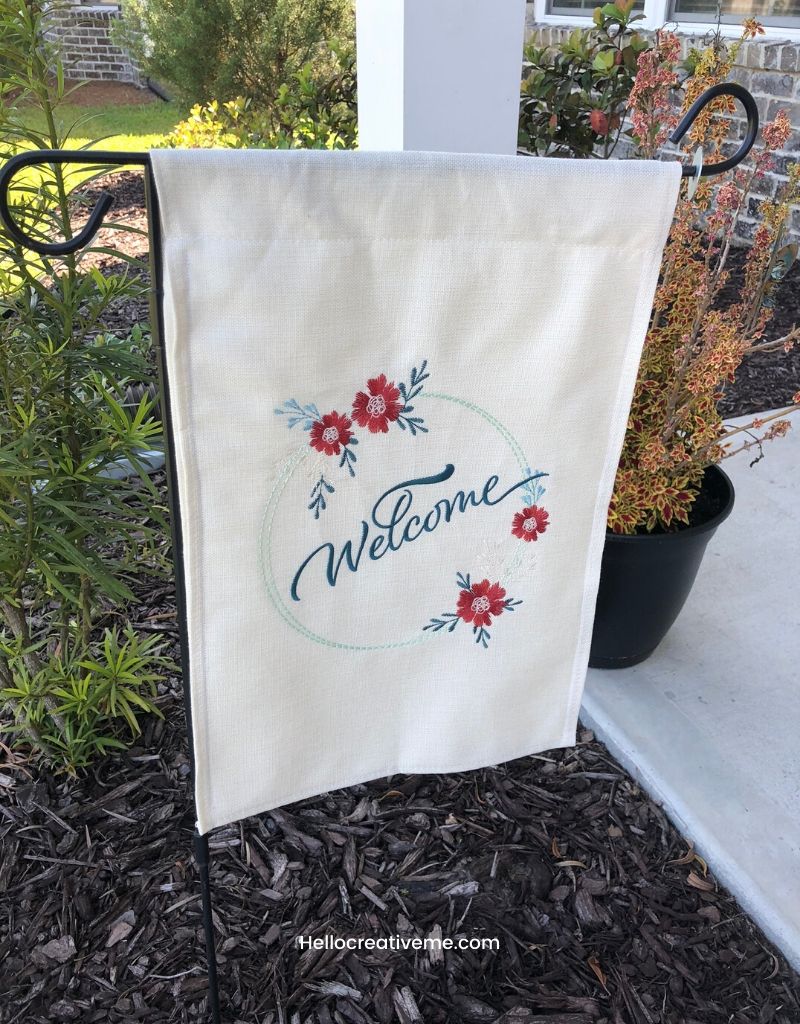 Off white embroidered garden flag that says welcome next to spring front porch.