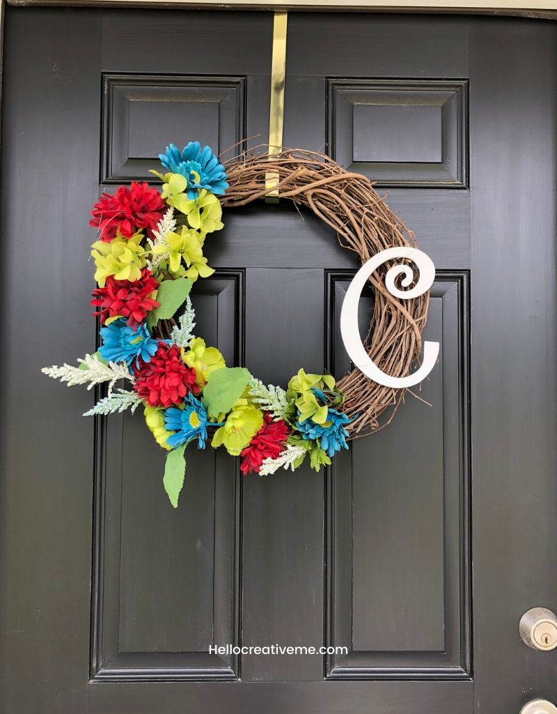 Grapevine door wreath with burgundy, green, cream and blue flowers and the initial C on a black door.
