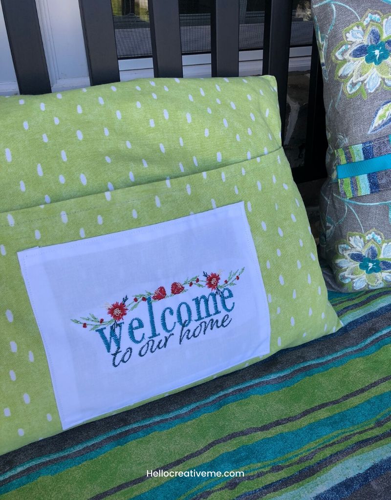 Green lumbar pillow with embroidered welcome to our home panel.