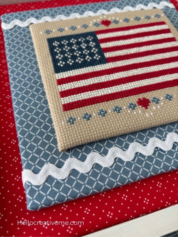 DIY cross stitch project mounted on layered fabric covered boards for display inside a frame.