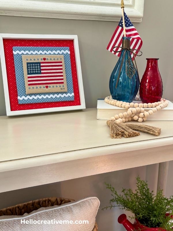 Framed DIY cross stitch of American flag used as tabletop display for patriotic home decor.
