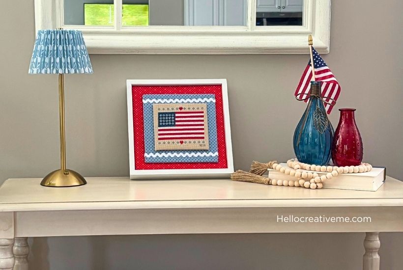 DIY American flag cross stitch finished in a frame and displayed on a tabletop.