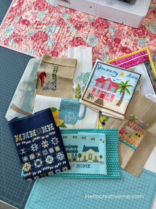 Group of unfinished cross stitch projects scattered on table waiting to be framed and displayed.