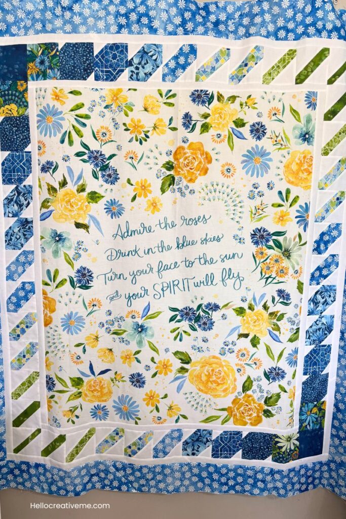 Finished quilt top with center panel with quote surrounded by blue and yellow roses and other flowers.