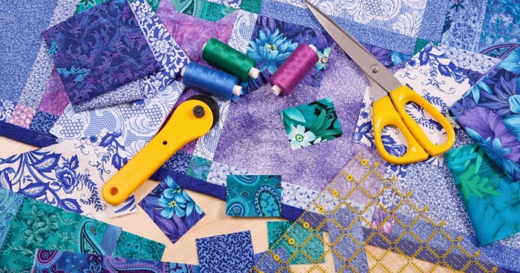 Quilting fabrics, thread, and cutting tools on a table.